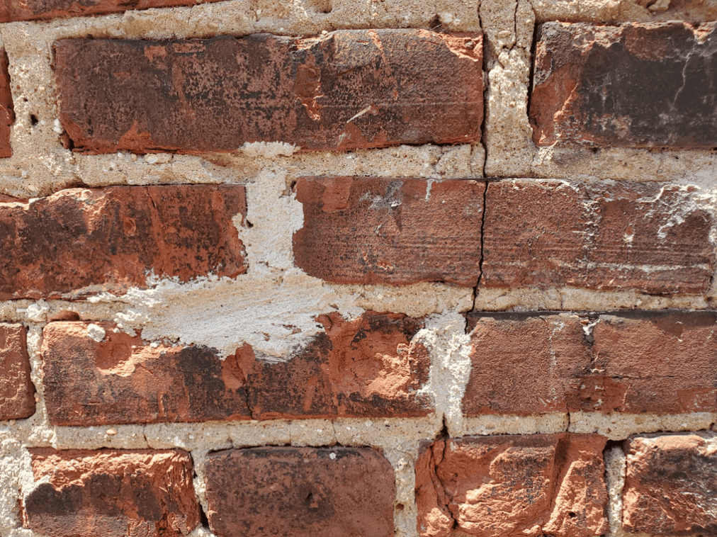 Historic brick wall with hard, incompatible mortar repairs causing cracking and moisture trapping in the masonry.