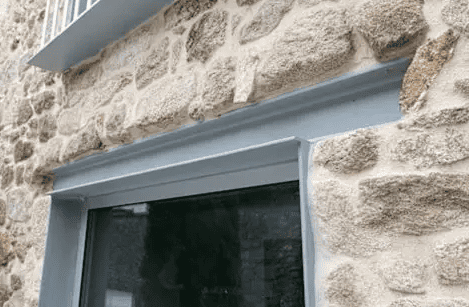 A modern grey metal window frame set against a rough, textured stone wall.