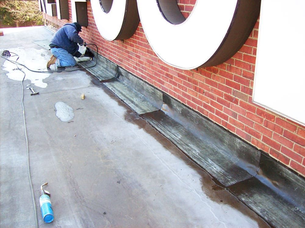 Contractor installing flashing and waterproofing at brick wall base to prevent water intrusion.