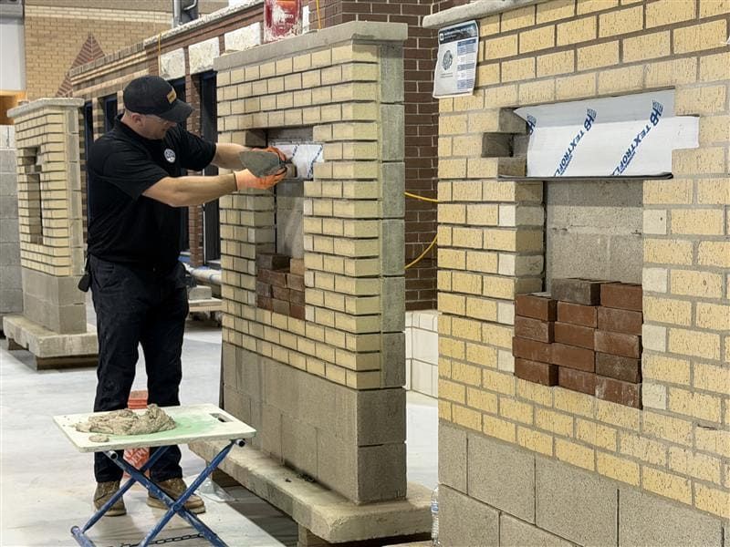 Worker installing bricks on a wall at a construction site, standing on a small step stool.