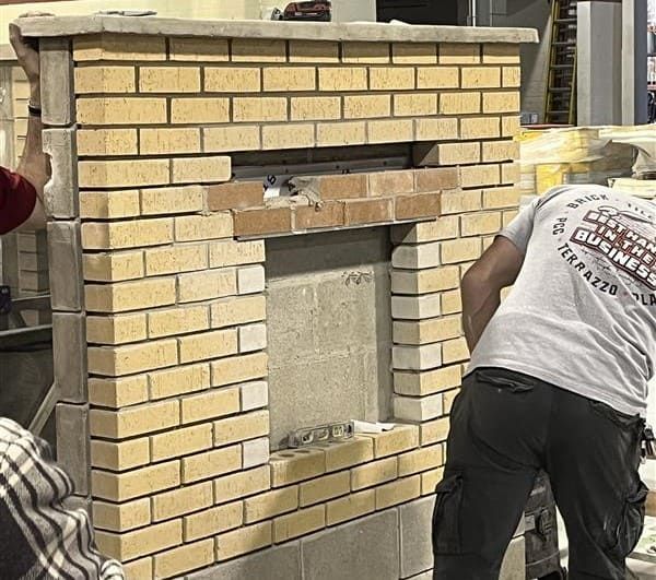 Workers installing tan brick veneer on a wall frame