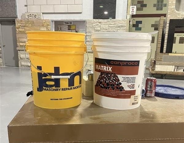 Two buckets on a table, one yellow and one white, with labels visible indoors.