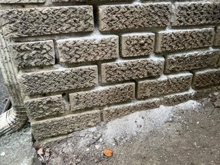 Close-up of masonry wall showing signs of mortar deterioration and granular debris at the base, indicating ongoing masonry joint failure.
