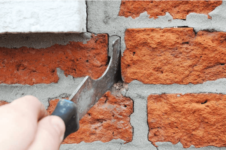 Hand trowel scraping mortar from a red brick wall during repair