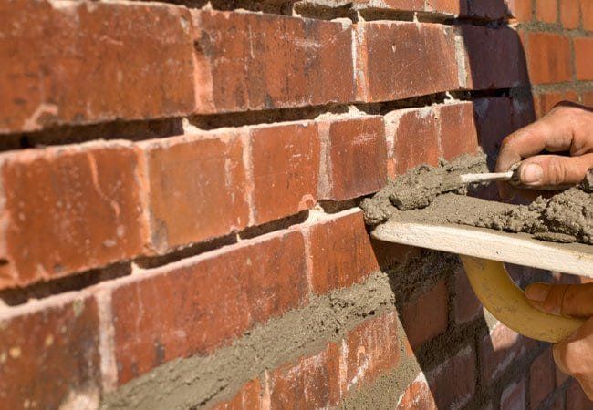 Bricklayer applying mortar to brick wall with a trowel.