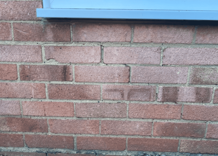 A close-up of a red brick wall with a hairline crack in the mortar below a light blue window frame.