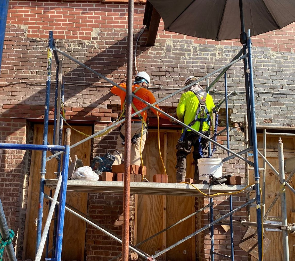 two construction workers doing masonry repair on a  brick building.