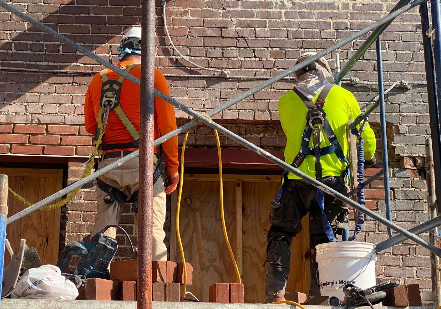 Two construction workers are working on a brick wall on a scaffolding.