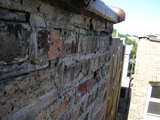 A close-up, high-angle view of a weathered brick wall and ledge, showing signs of deterioration and crumbling mortar.