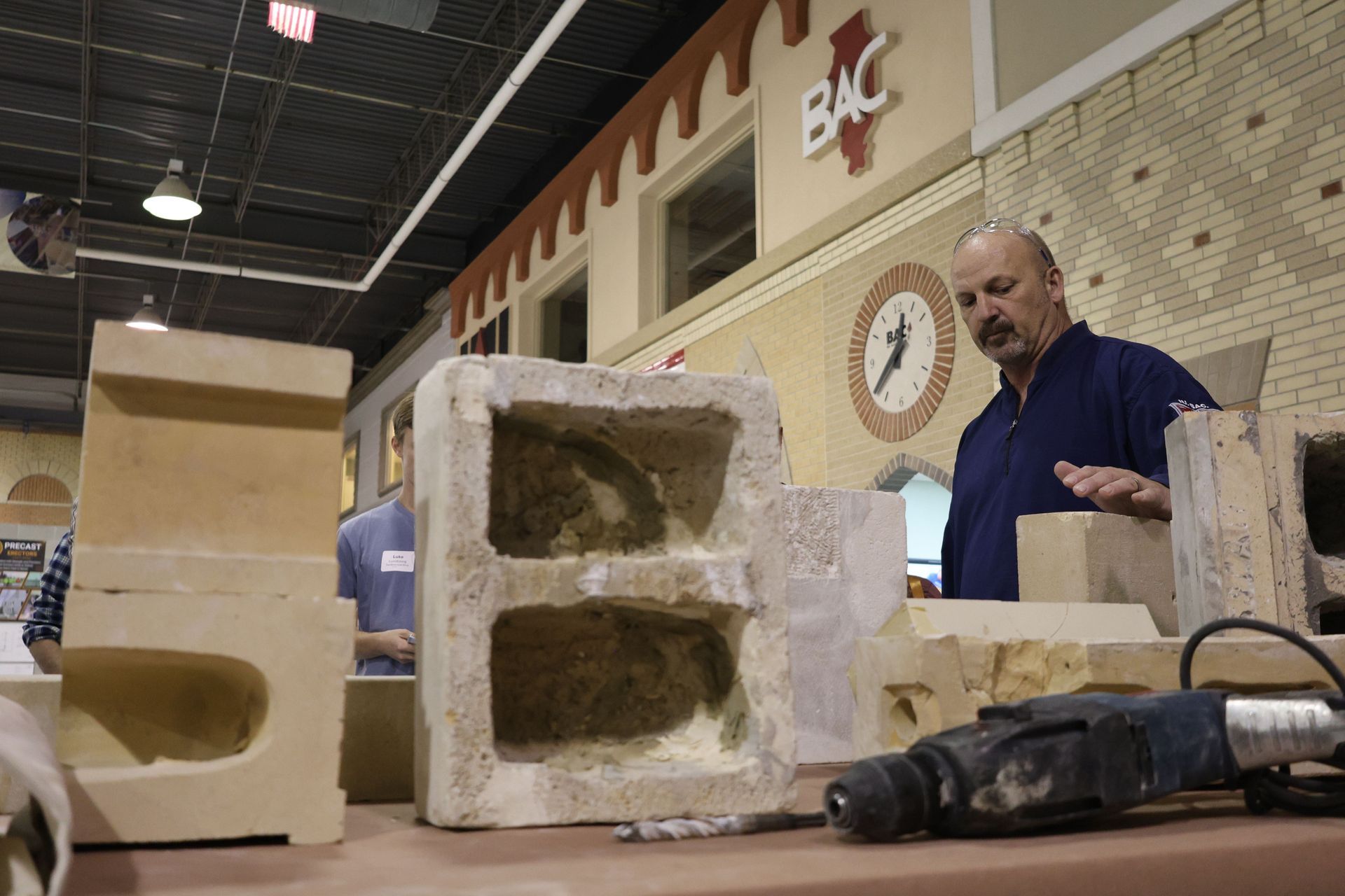 Instructor standing behind various damaged masonry units and repair samples during a workshop