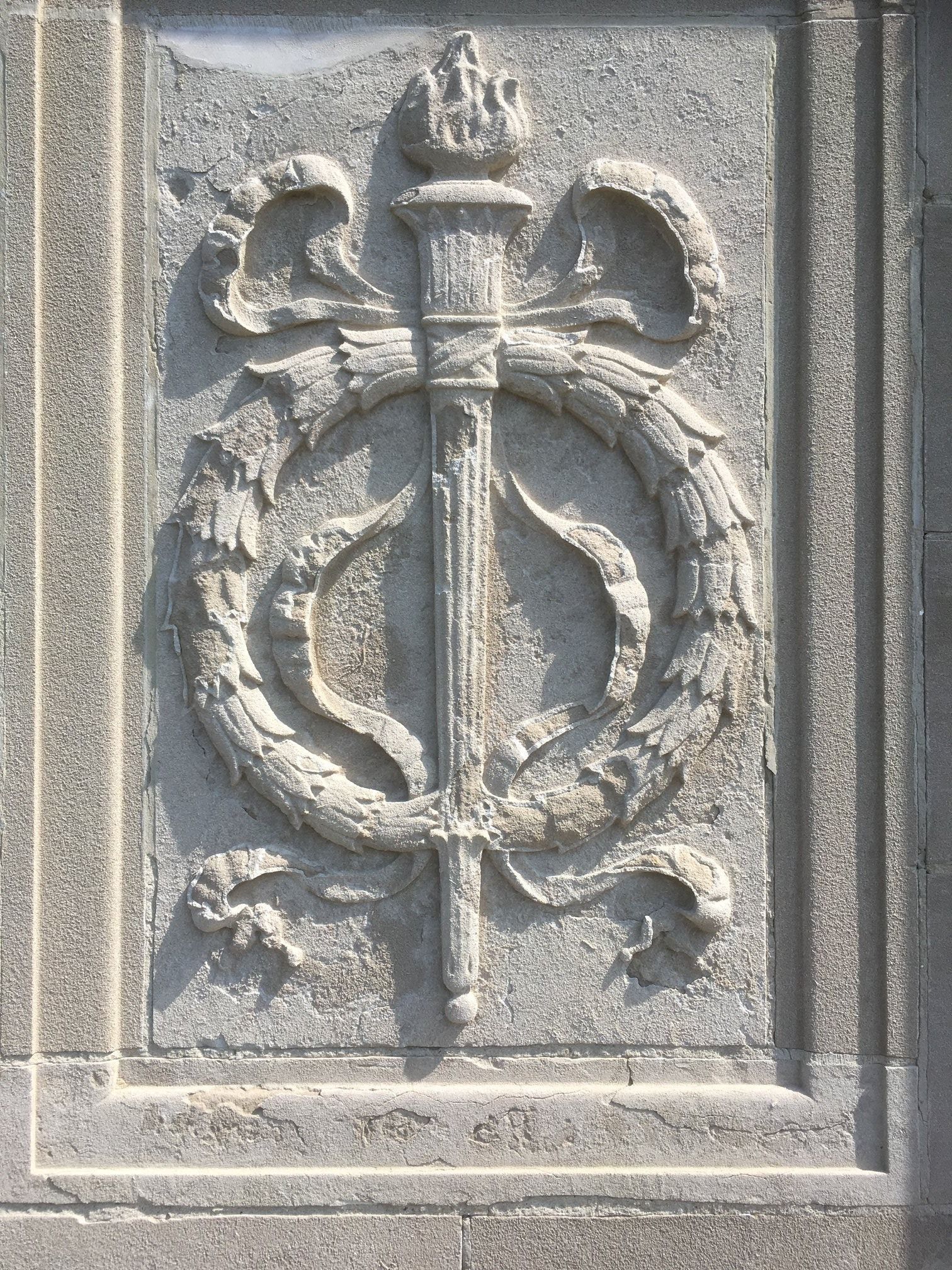 A stone carving of a torch with a wreath around it