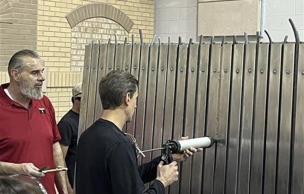 IMI instructor guiding a participant through proper sealant installation techniques at the hands-on sealant station during the masonry restoration workshop in Addison, Illinois.