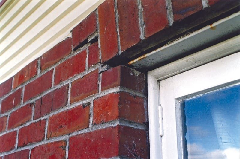 : Rusted steel lintel expanding and causing brick displacement and cracking above a window — example of a common winter masonry failure.