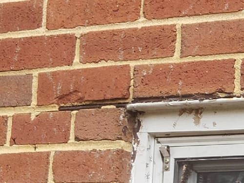 Close-up of a rusted steel lintel above a window with visible staining and masonry cracking caused by moisture exposure and winter freeze–thaw conditions.
