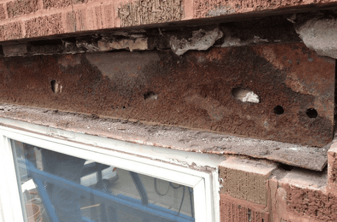 A rusted steel lintel supporting a brick wall above a white window frame, showing significant corrosion and decay.