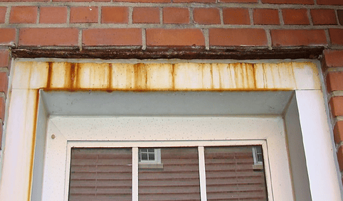 Corroded steel window lintel with rust staining on brick façade caused by water intrusion from failed expansion joints.