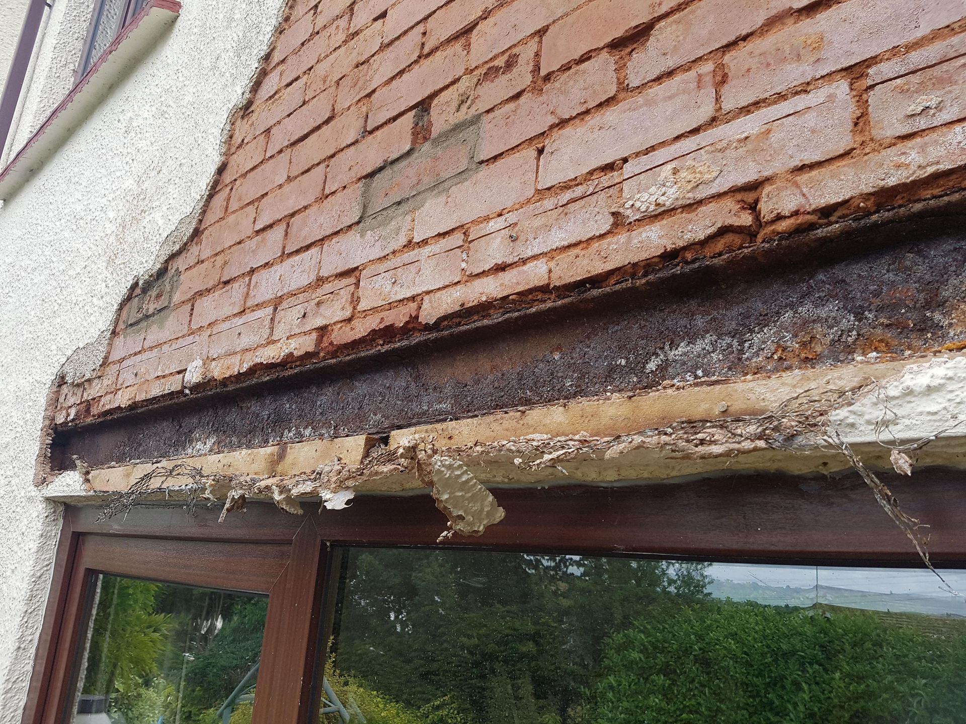 Exposed and rusted steel lintel beneath deteriorating brick masonry above a window, showing structural damage caused by moisture intrusion.