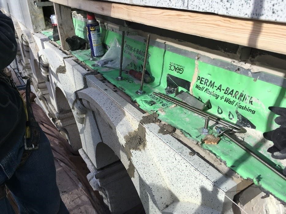 A construction site showing concrete block walls with a green Perm-A-Barrier membrane and metal reinforcing bars.