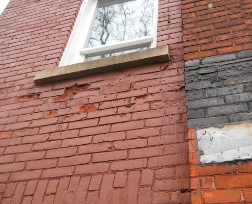 Spalling brick on a painted masonry facade below a windowsill.