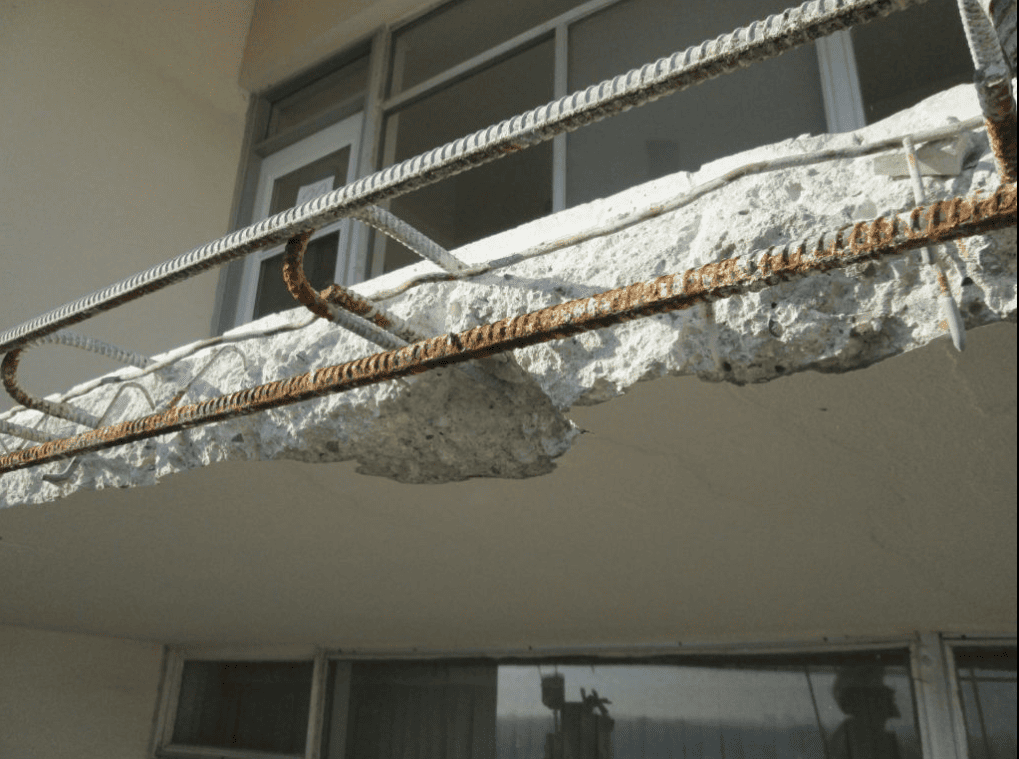 Spalled concrete balcony with exposed reinforcing steel and rust staining resulting from moisture intrusion and freeze–thaw damage.