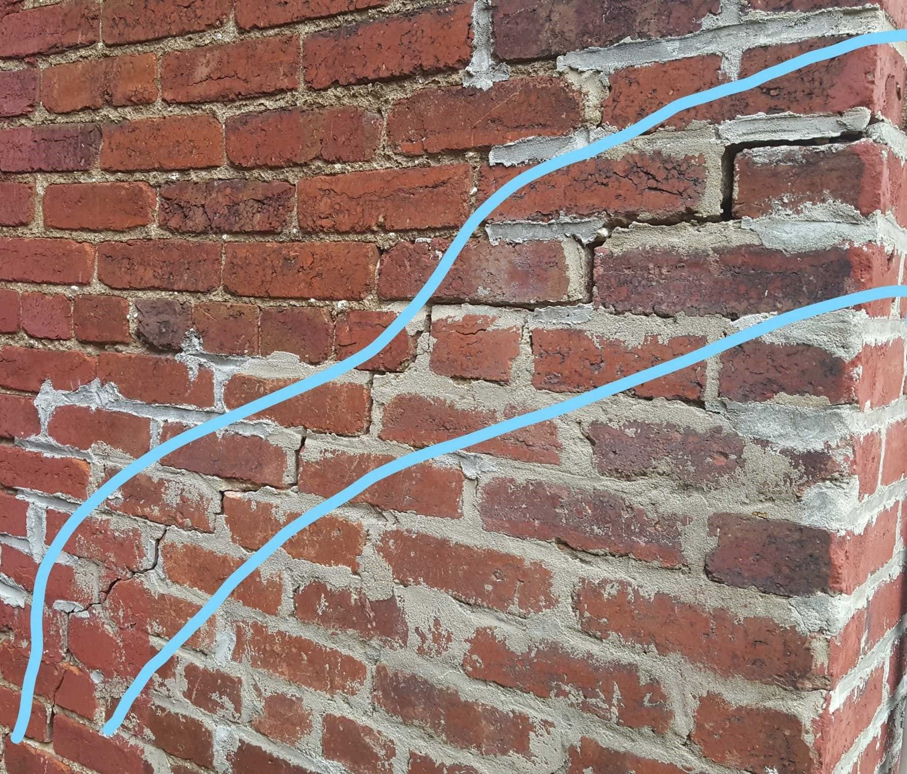 A close-up of a red brick wall showing cracks along the mortar lines, highlighted by two faint blue lines.