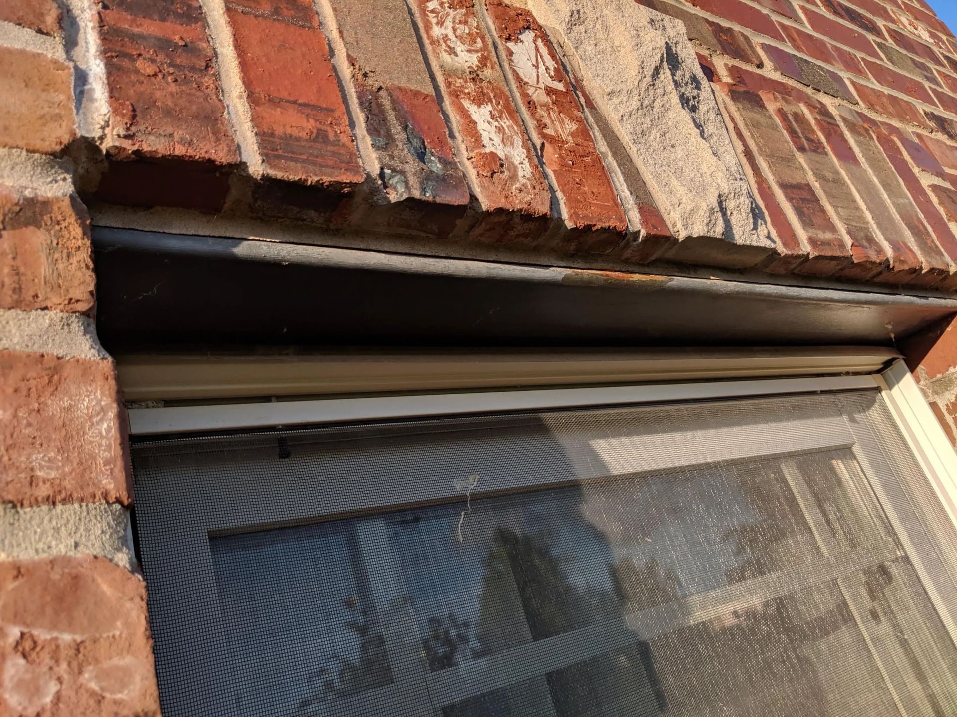 Steel lintel corrosion above a brick window opening with rust staining and masonry deterioration caused by trapped moisture and flashing failure.