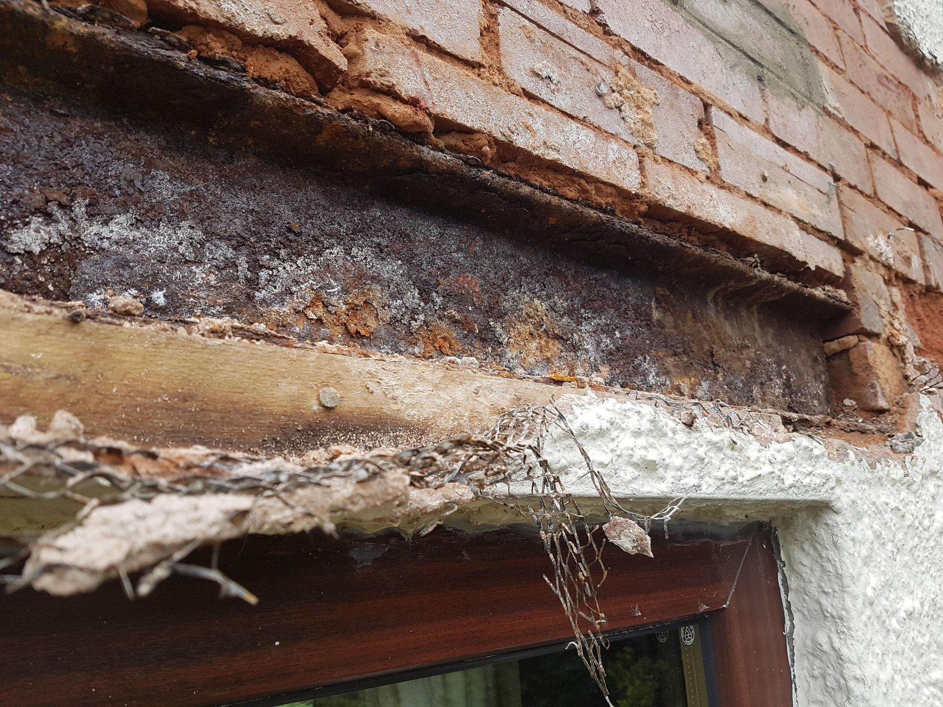 Damaged brick wall with crumbling wood and water damage above a window frame