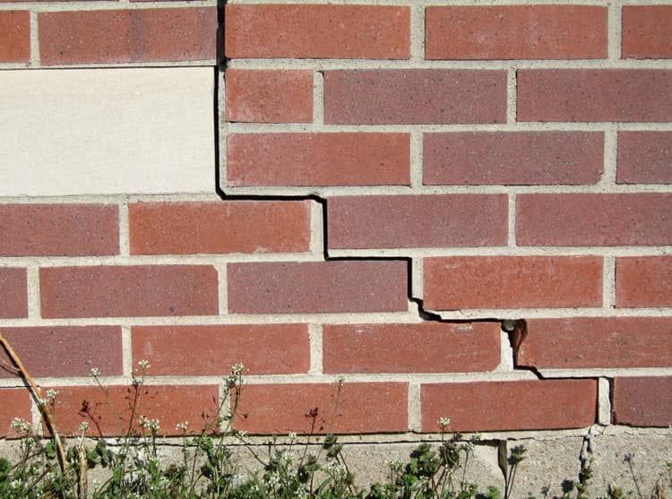 Stair-step brick cracking near a window opening caused by freeze–thaw movement and lintel stress in a masonry wall.