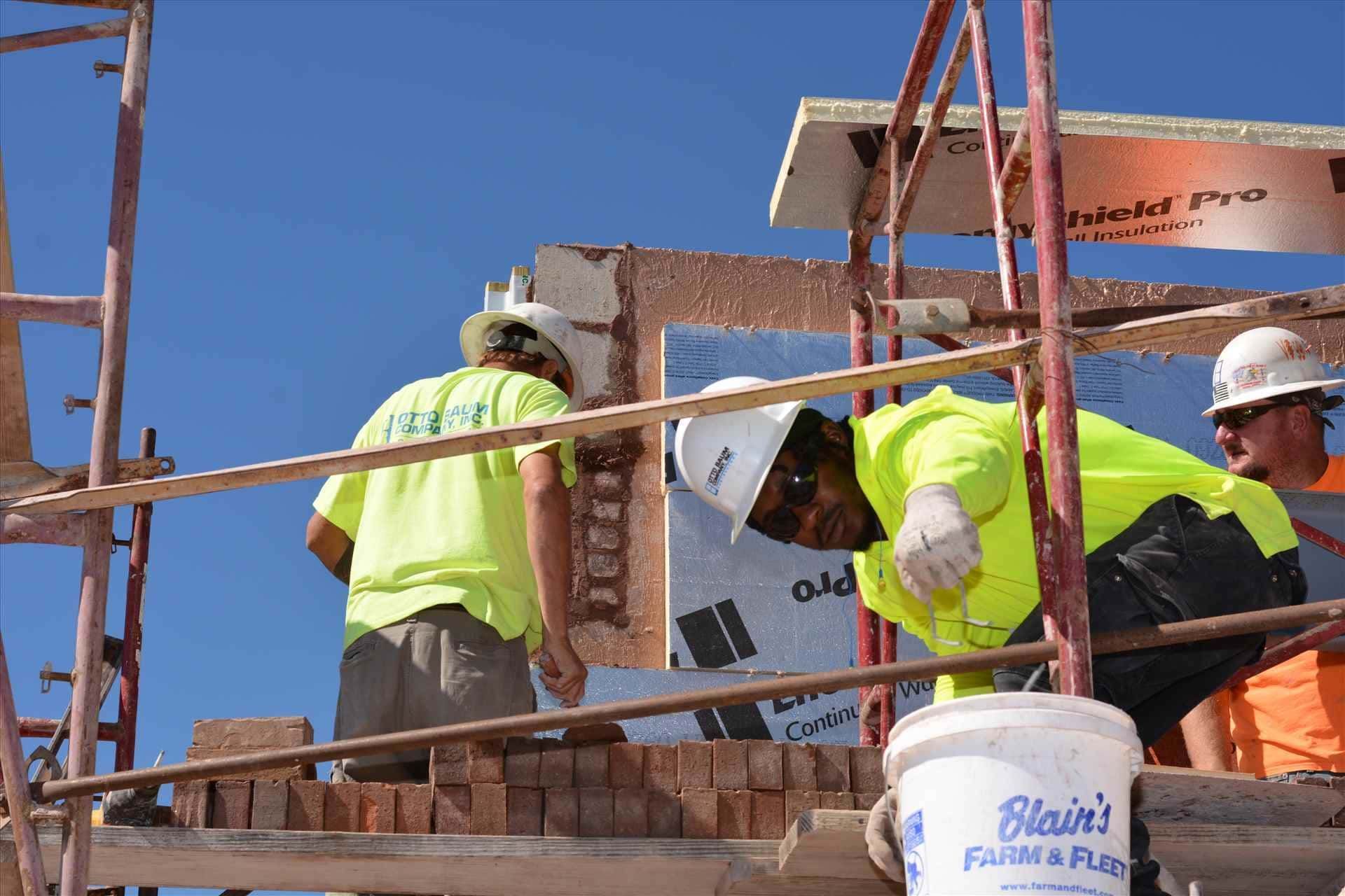 Construction workers installing a large sign on a building scaffold under a clear blue sky