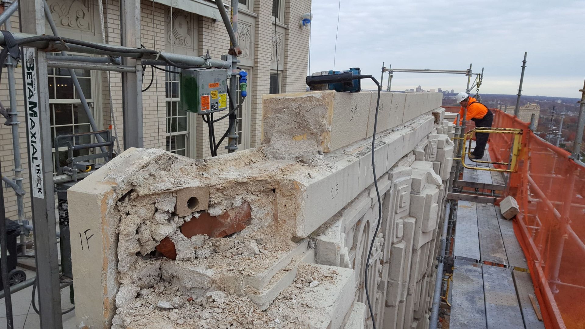 Restoration in progress with masons repairing mortar joints and securing historic terra cotta facade to prevent further deterioration.