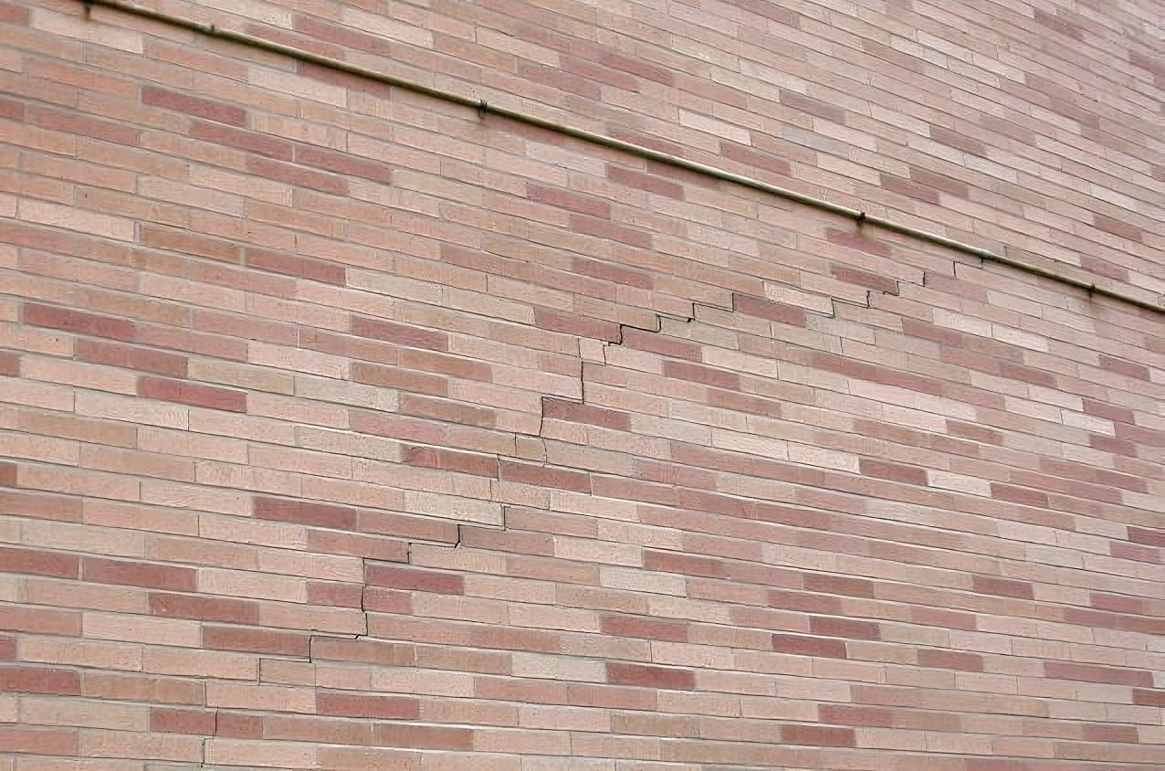 Brick wall with visible stair-step cracking caused by thermal expansion, showing how heat and temperature changes can stress masonry structures over time.