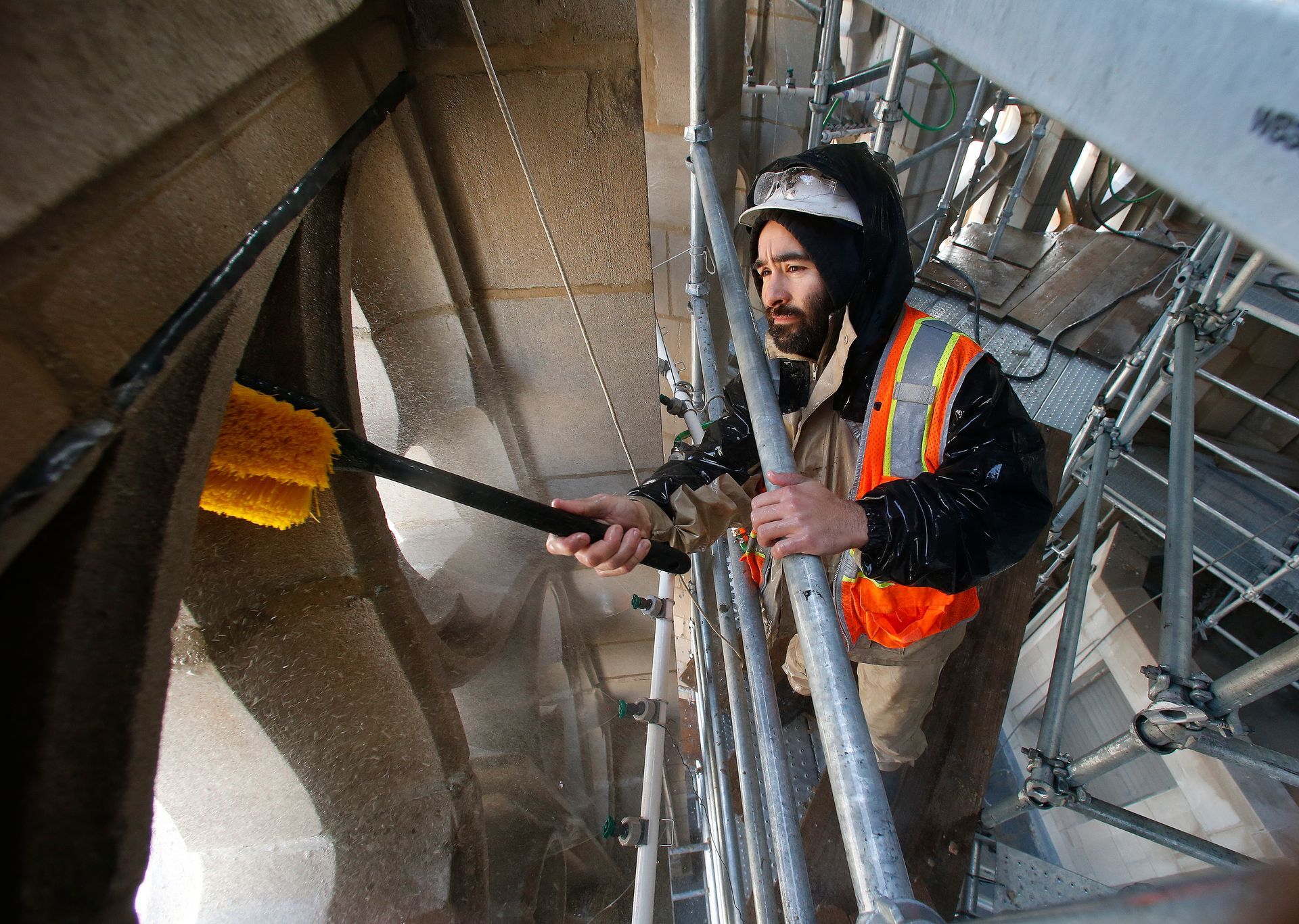 A man in an orange vest is cleaning a building with a brush