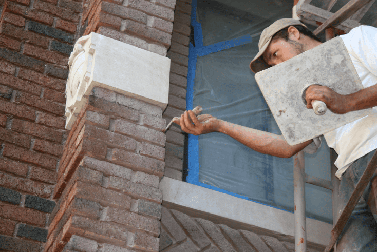 Mason performing detailed tuckpointing work on decorative brick facade using hand tools.