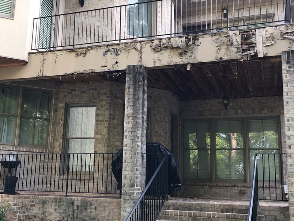 Water-damaged balcony with deteriorated framing and adjacent masonry indicating broader building envelope issues