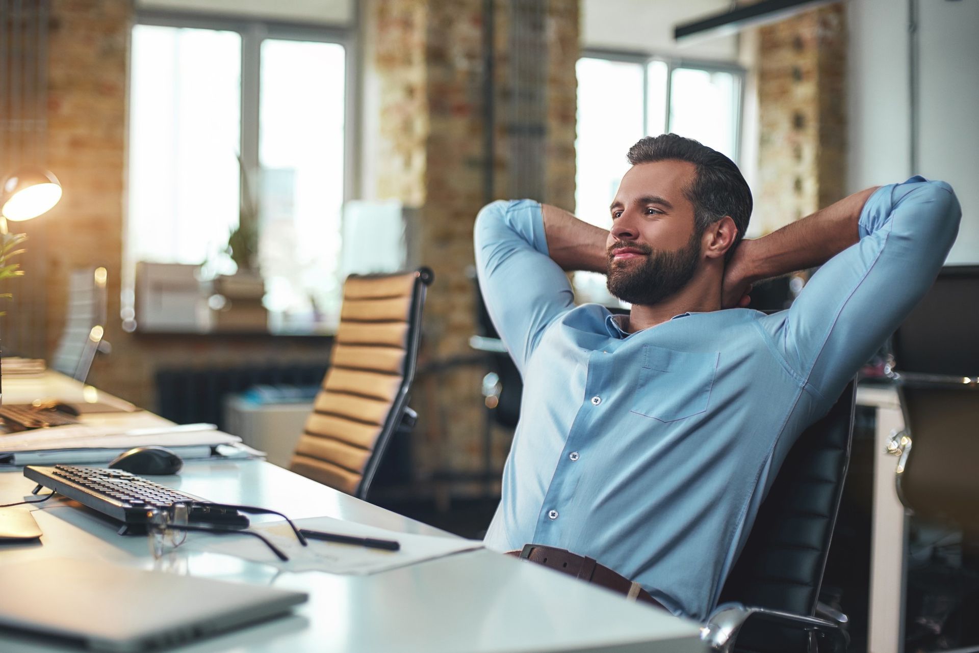 Man leaning back in office chair, hands behind head, smiling.