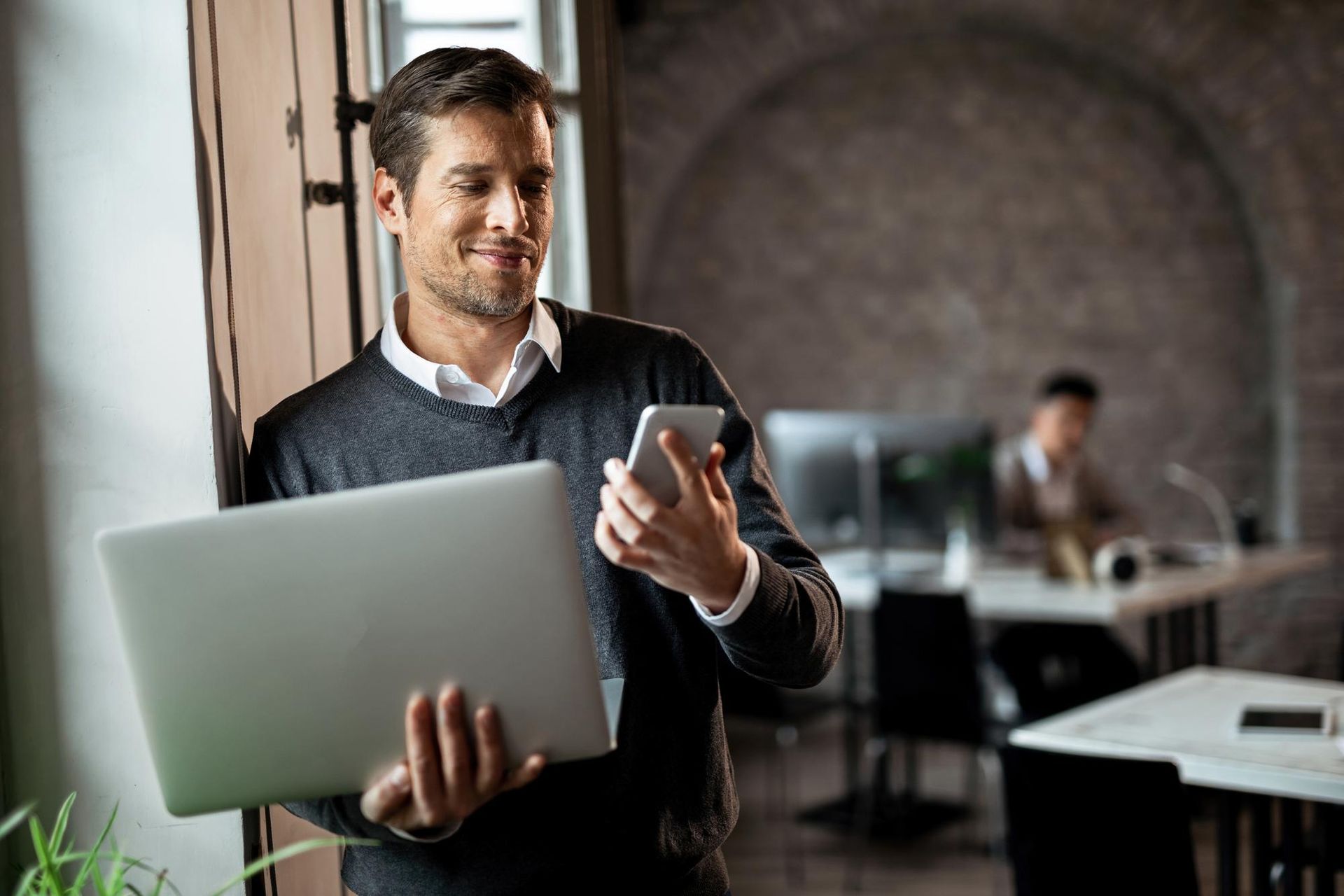 A man is holding a laptop and a cell phone.