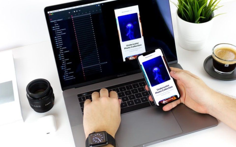 A person is typing on a laptop and holding a cell phone.