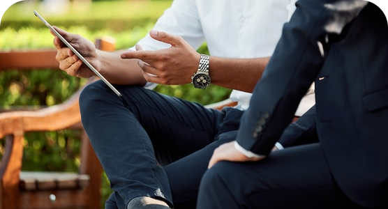 Two men are sitting on a bench looking at a tablet.