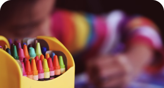 A child is drawing with crayons in a yellow box.
