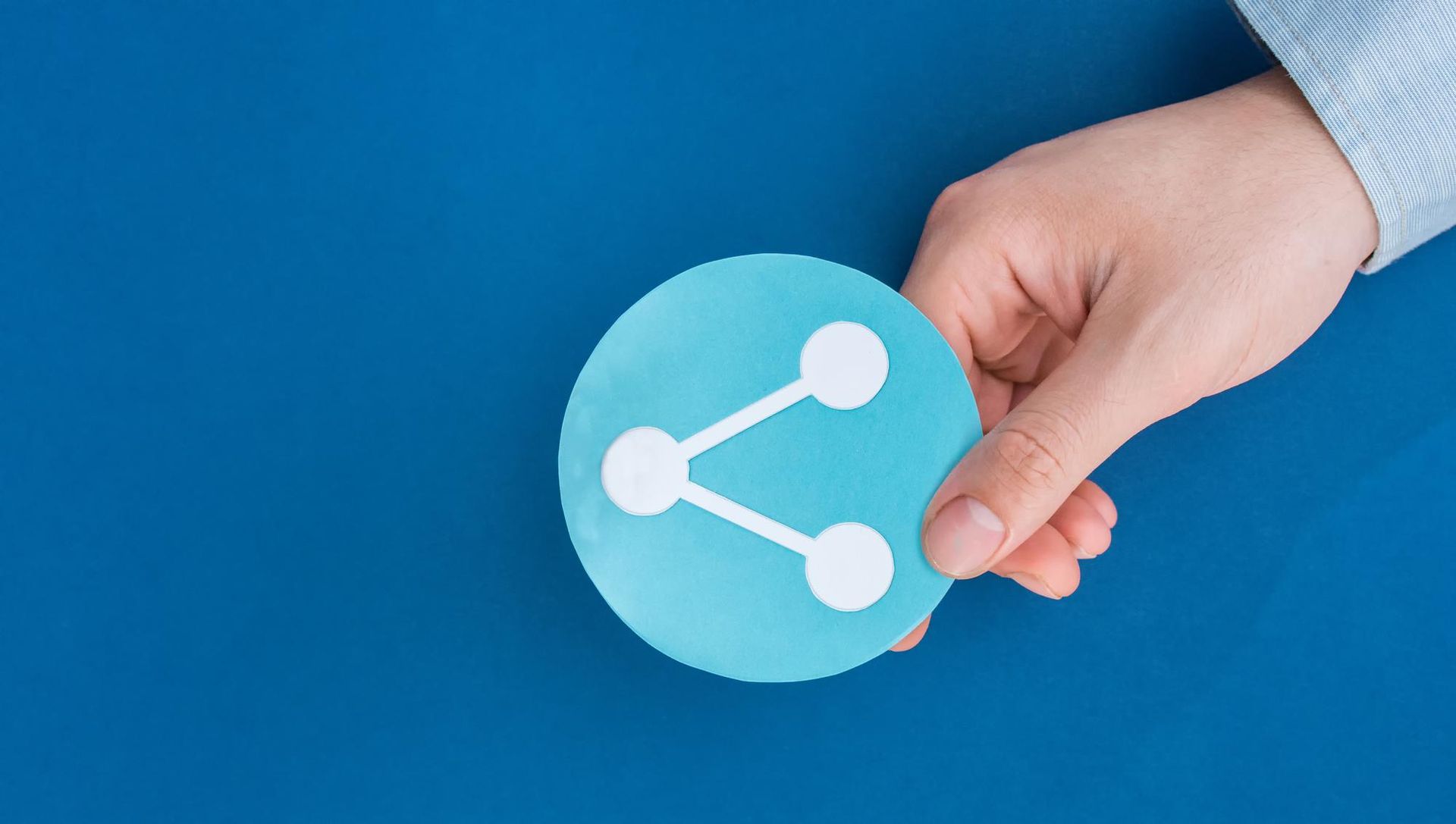 A person is holding a blue circle with a share icon on it.