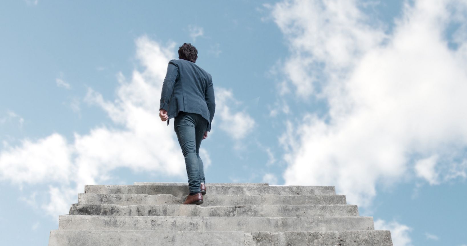 A man is walking up a set of stairs towards a cloudy sky.
