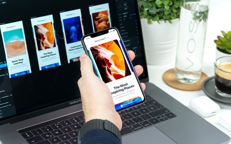 A person is holding a cell phone in front of a laptop.
