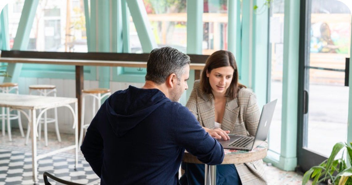A man and a woman are sitting at a table looking at a laptop.