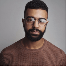 A man with a beard and glasses is wearing a brown sweater.