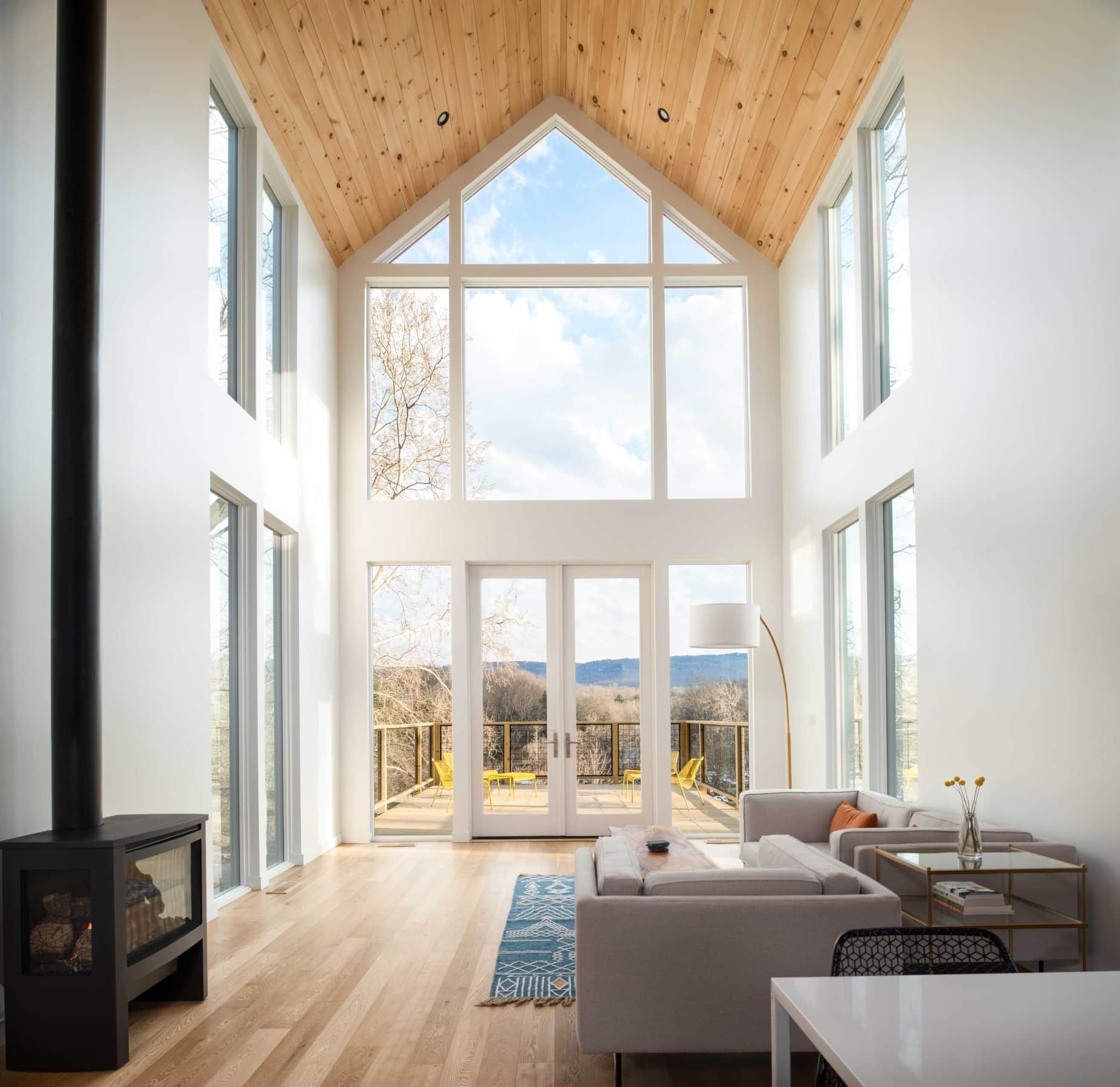 Bright modern living room with soaring wood ceiling, tall windows, sofa, and mountain view.