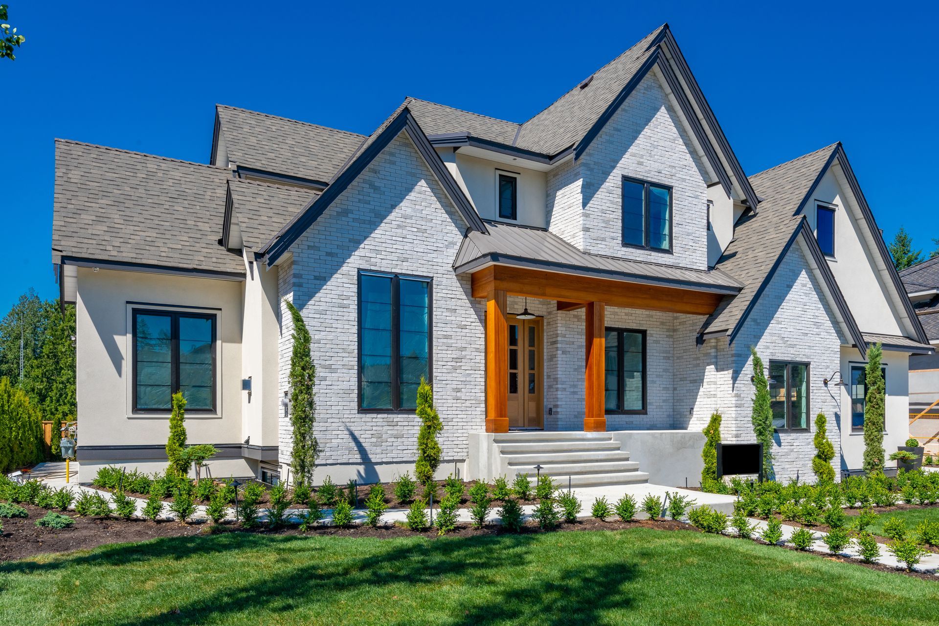 A large white house with a gray roof is sitting on top of a lush green lawn.