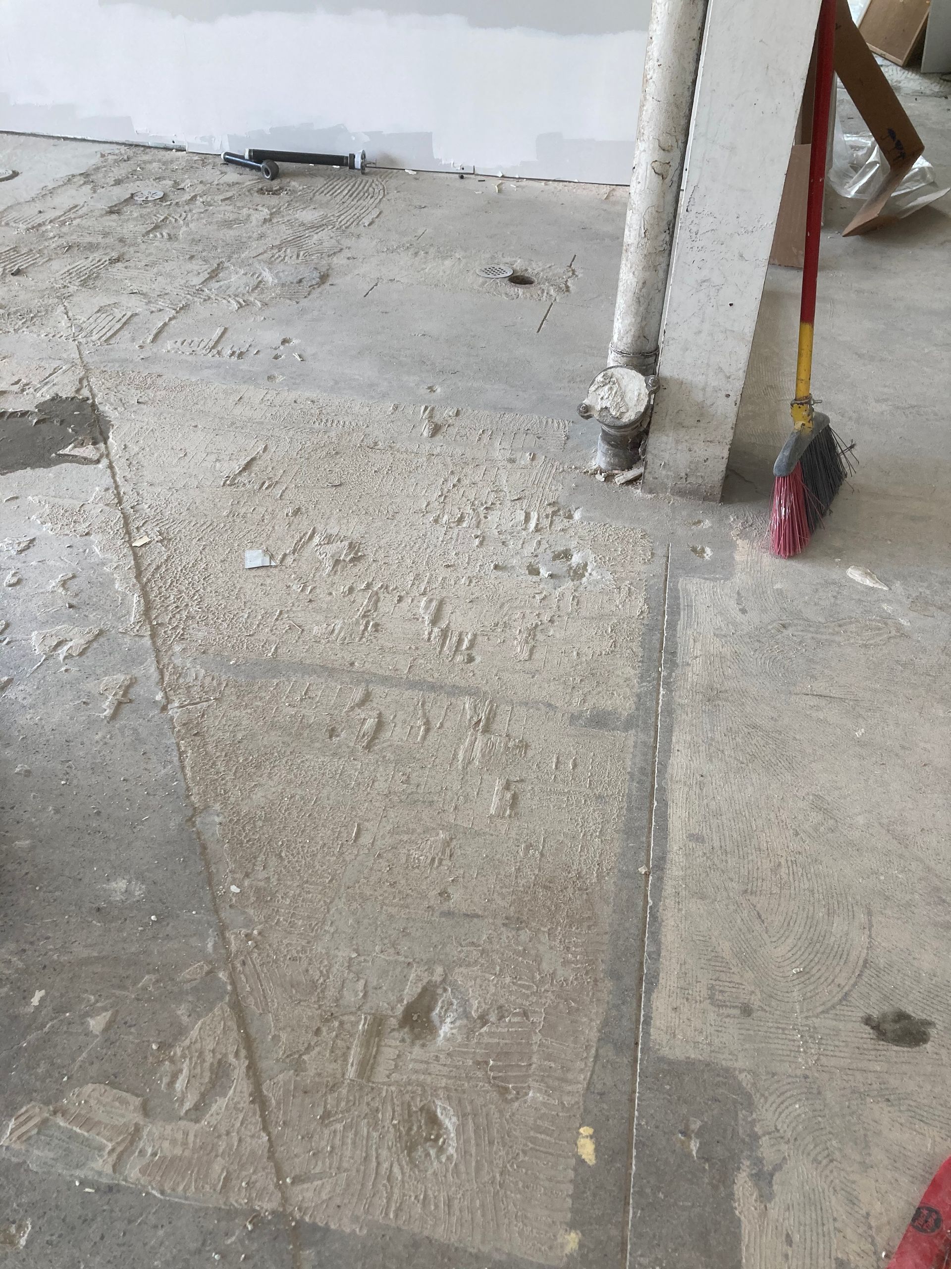 A broom is sitting on the floor next to a pipe.