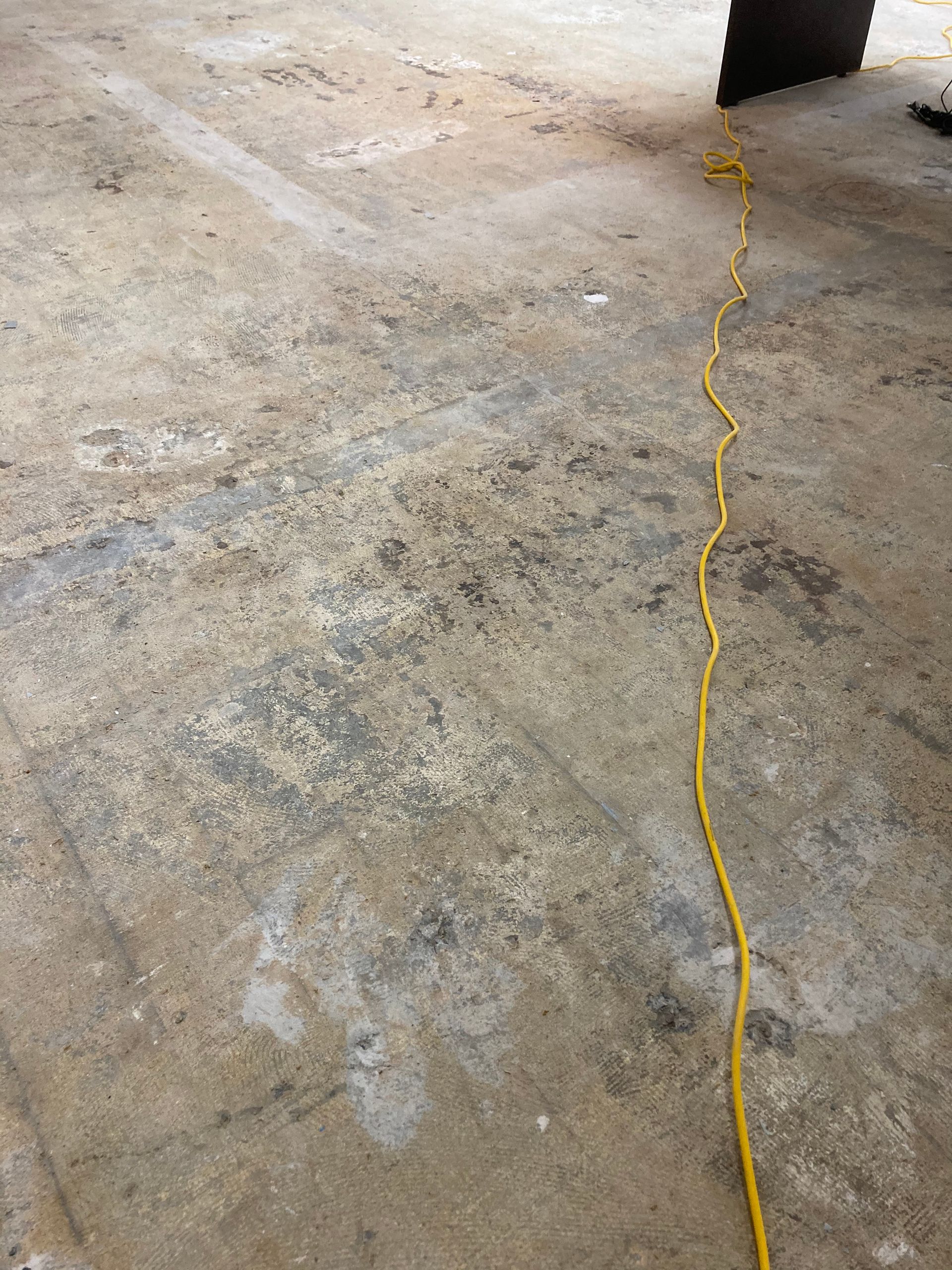 A yellow power cord is laying on a concrete floor.