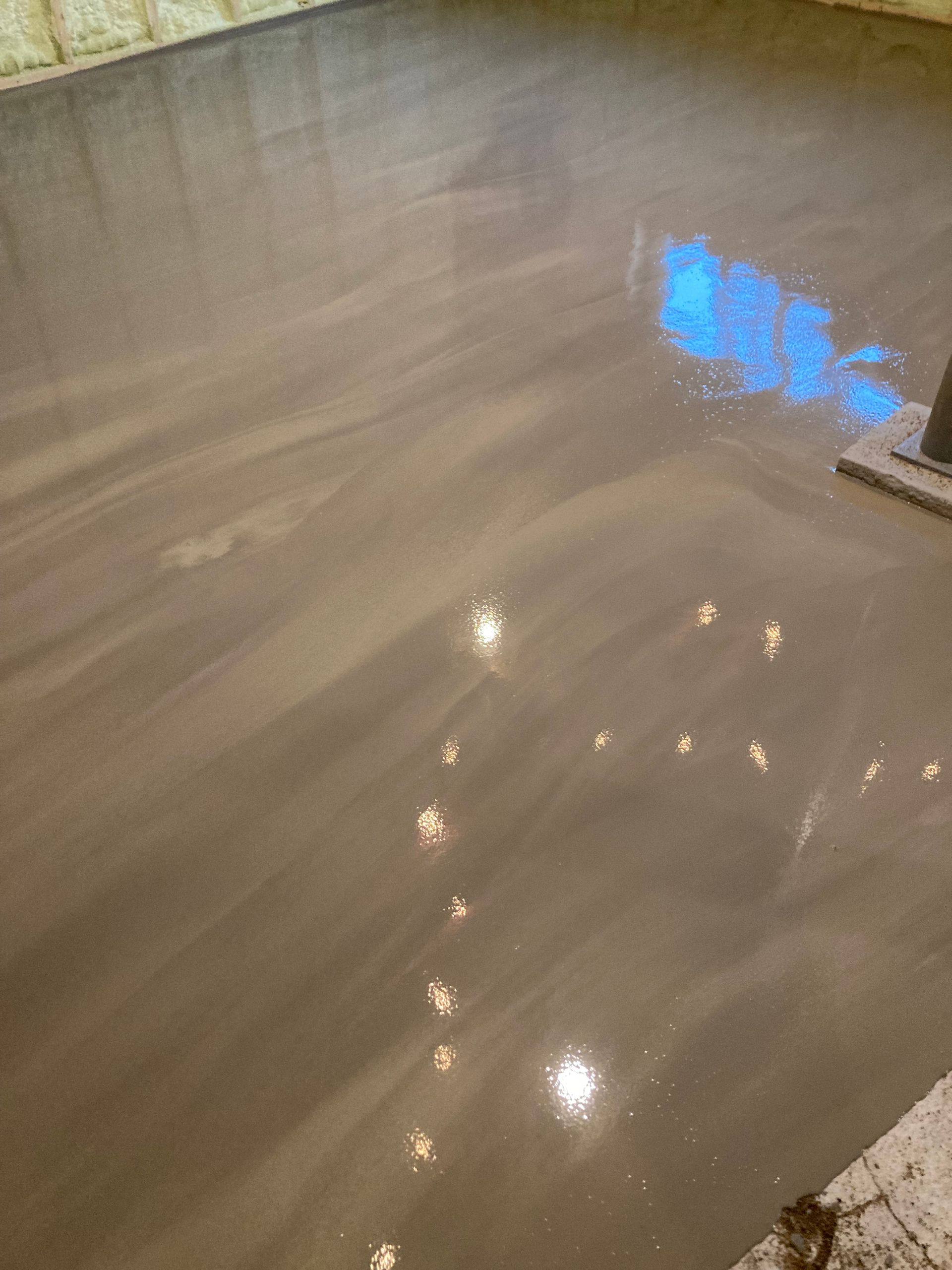 A close up of a concrete floor with a reflection of lights in it.