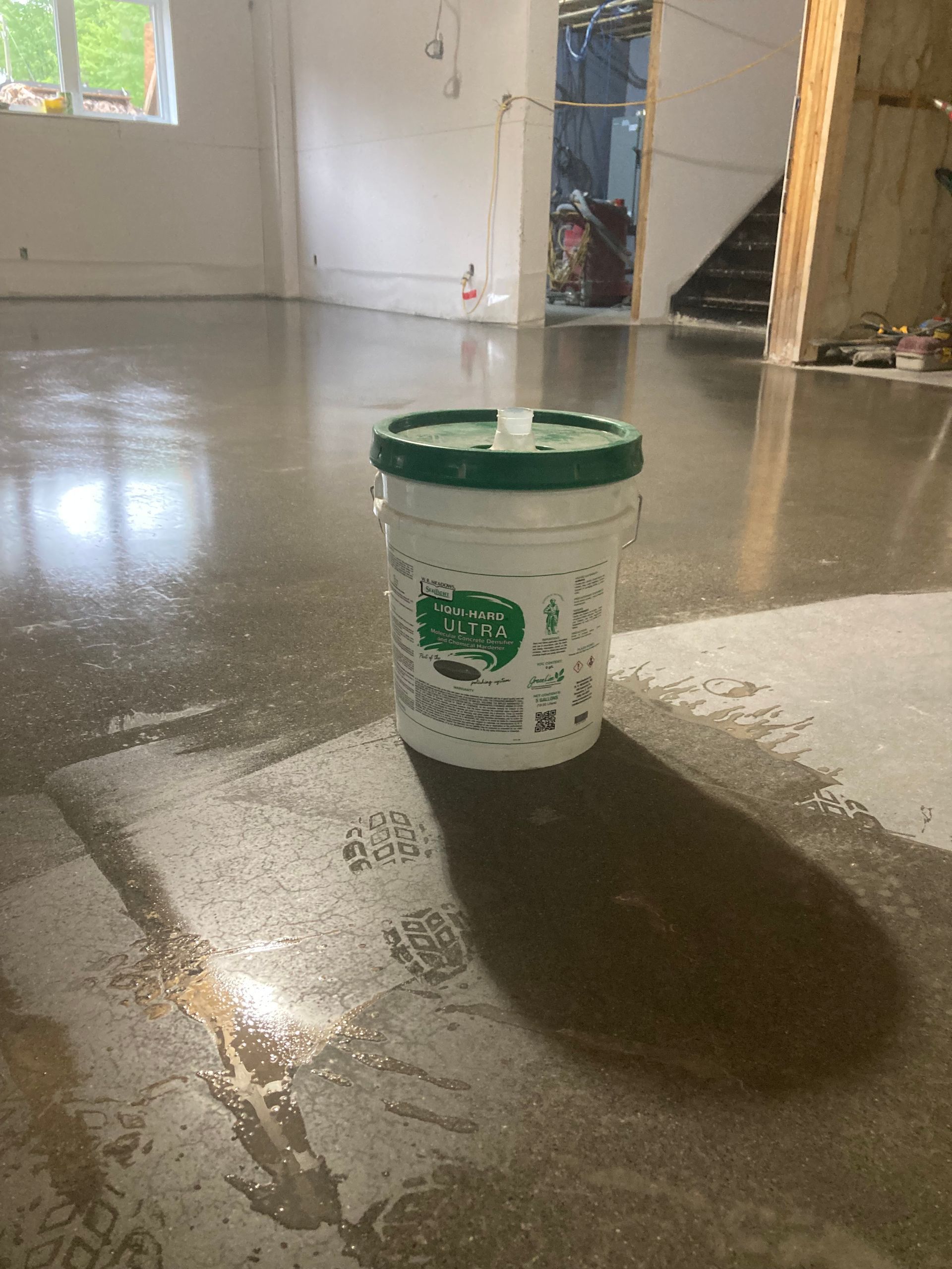 A white bucket with a green lid is sitting on a concrete floor.